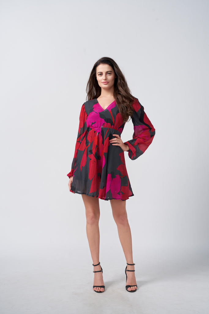 Model wearing a short chinon dress with red and pink abstract floral print, V-neck, and long puff sleeves.