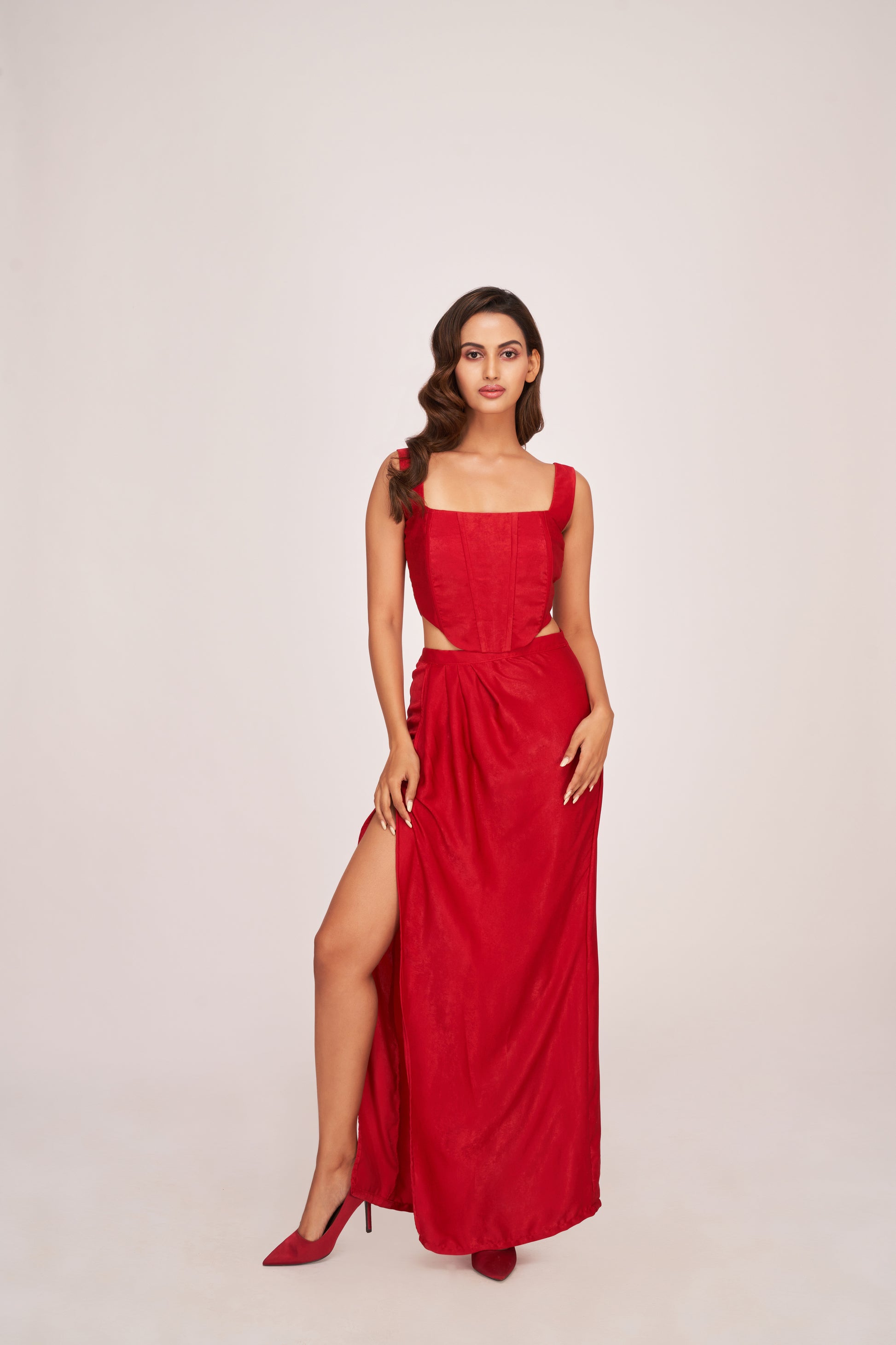 Model standing tall in a red suede velvet corset co-ord set, showcasing square neck and thigh-high slit skirt in a bold frontal pose.