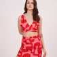 Model in a front-facing pose wearing the deep V-neck red printed co-ord set with sleeveless crop top and high-slit skirt.