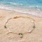 A delicate and feminine gold-toned anklet with a sparkling flower centerpiece and olive green accents, designed to add a graceful touch to your summer vacation.