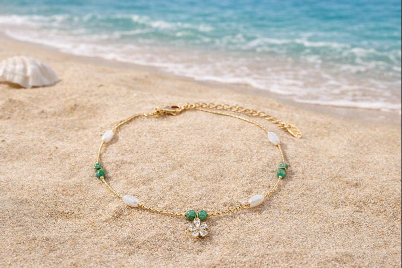 A delicate and feminine gold-toned anklet with a sparkling flower centerpiece and olive green accents, designed to add a graceful touch to your summer vacation.