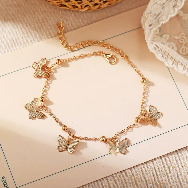 A delicate gold-toned anklet featuring high-shine butterfly charms with detailed wing cutouts, perfect for adding a whimsical and feminine touch to a summer party or wedding outfit.
