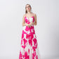 Model standing front-facing in a full-length pink and white floral dress with ruched front and spaghetti straps.
