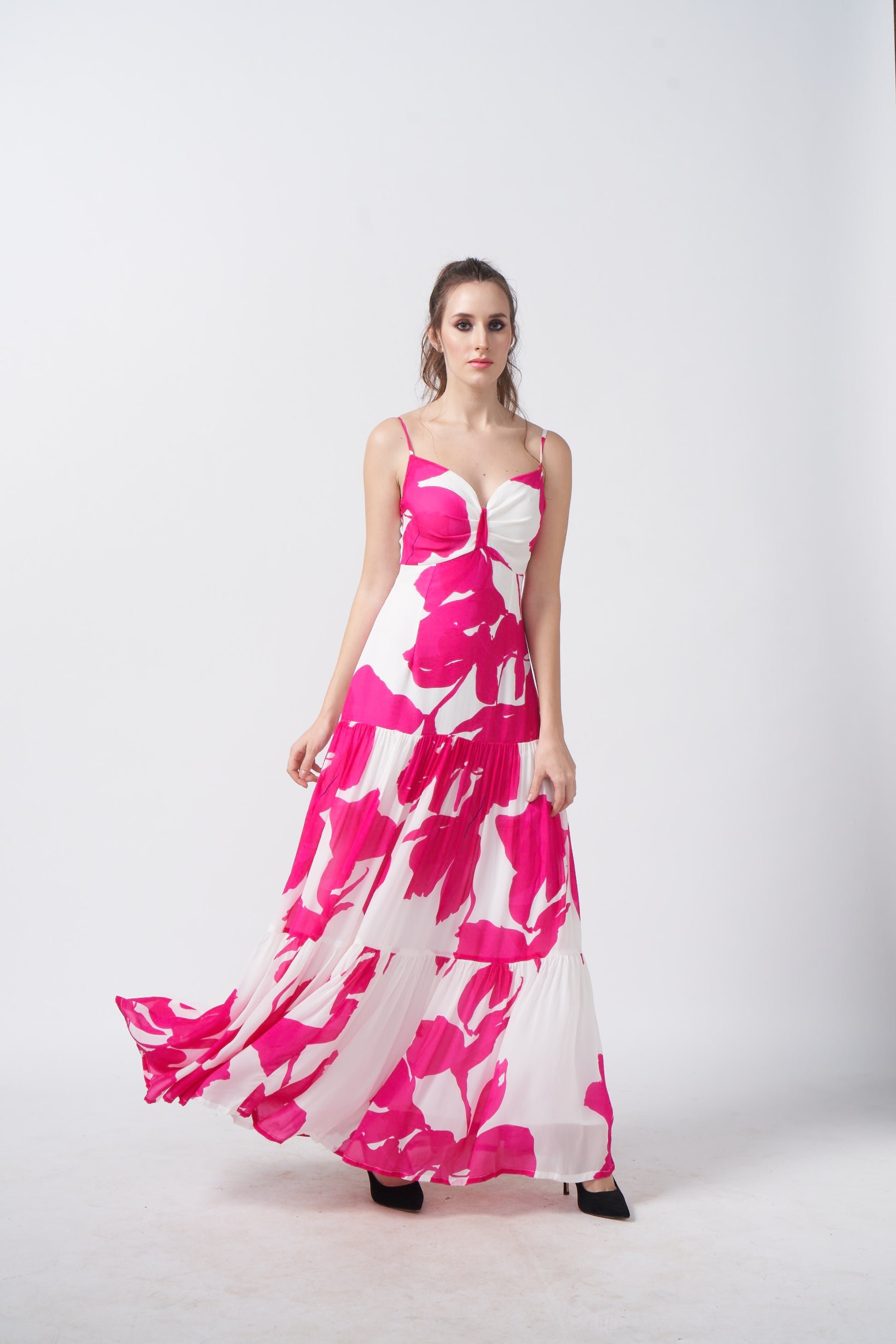 Walking pose of model in the ruched pink and white floral long dress.
