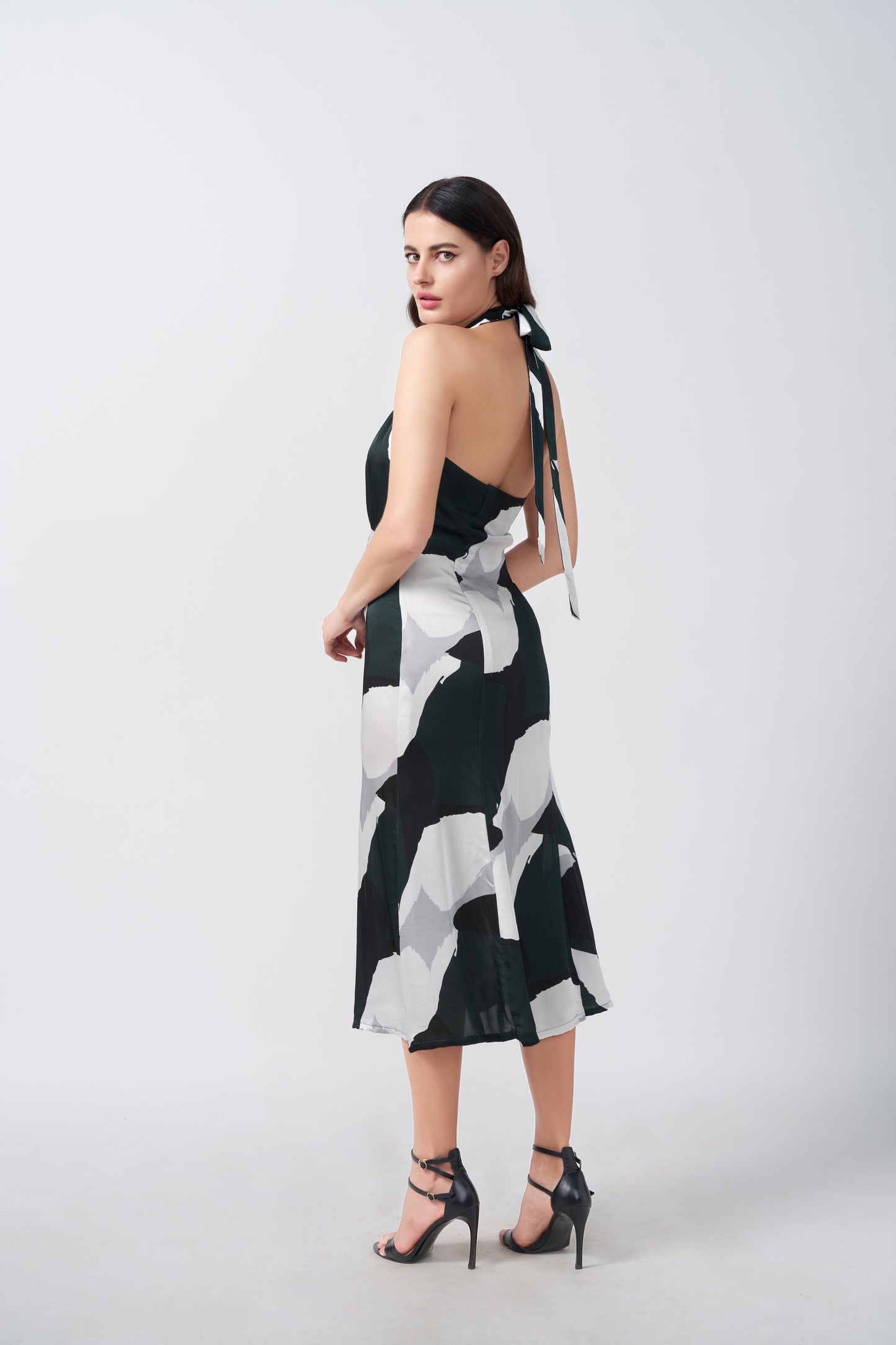 Side profile of model showing halter tie-back neck and silhouette of satin abstract print dress.