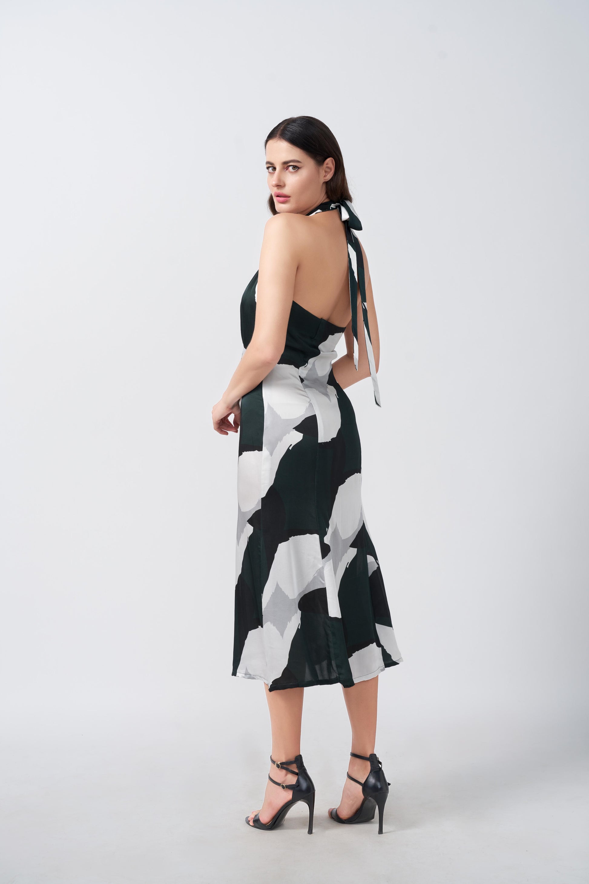 Side profile of model showing halter tie-back neck and silhouette of satin abstract print dress.