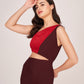 Angled view of model in brown and red panelled cut-out dress with one shoulder exposed, touching her head.