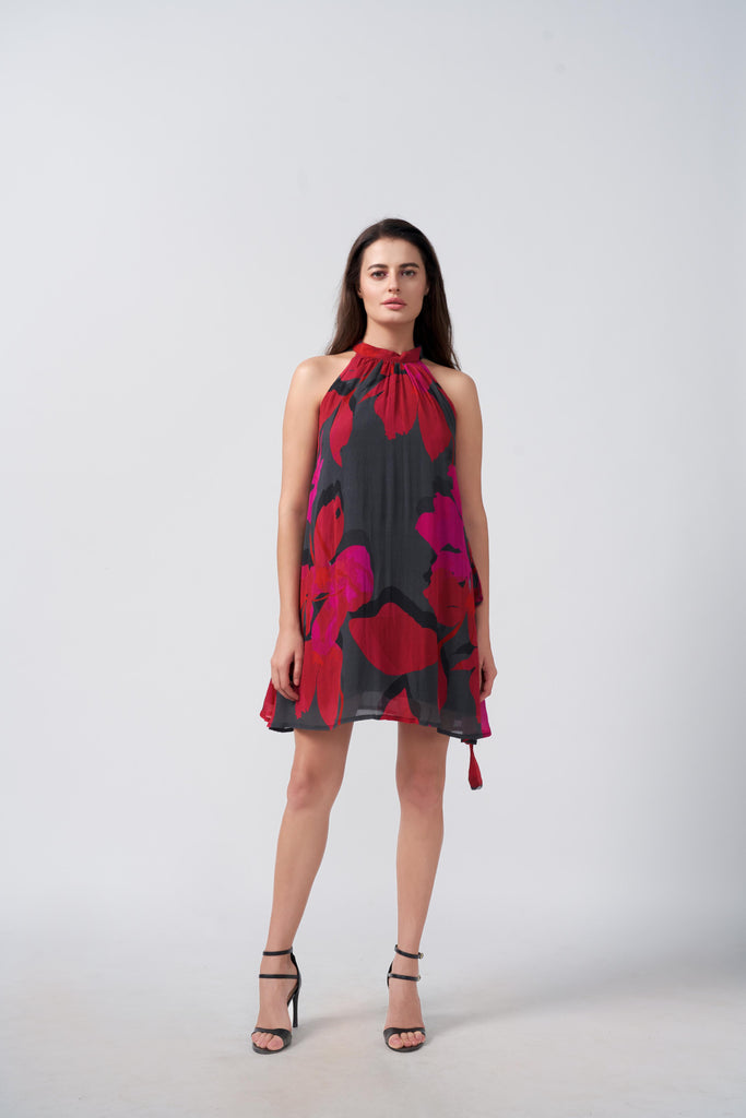 Model wearing a red and pink abstract floral halter dress with tie-back neck, standing in studio.