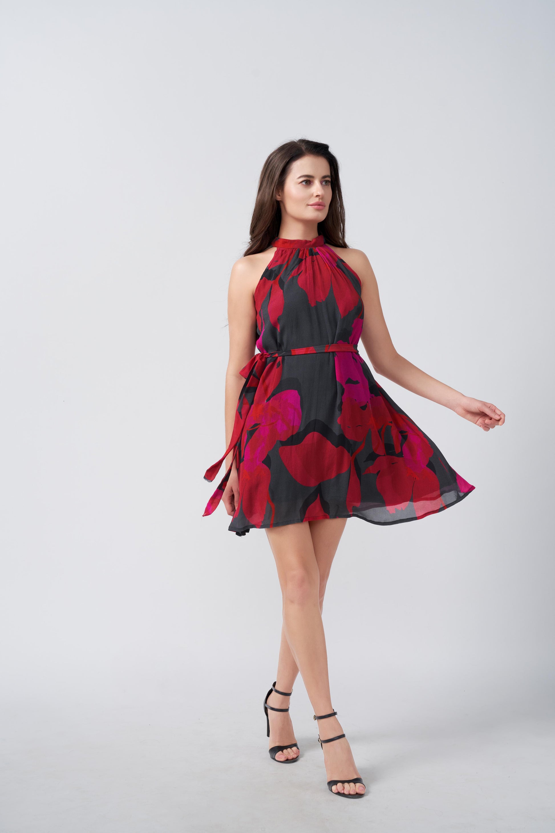 Model posing playfully in red and pink halter dress with flowy knee-length silhouette, facing slightly sideways.
