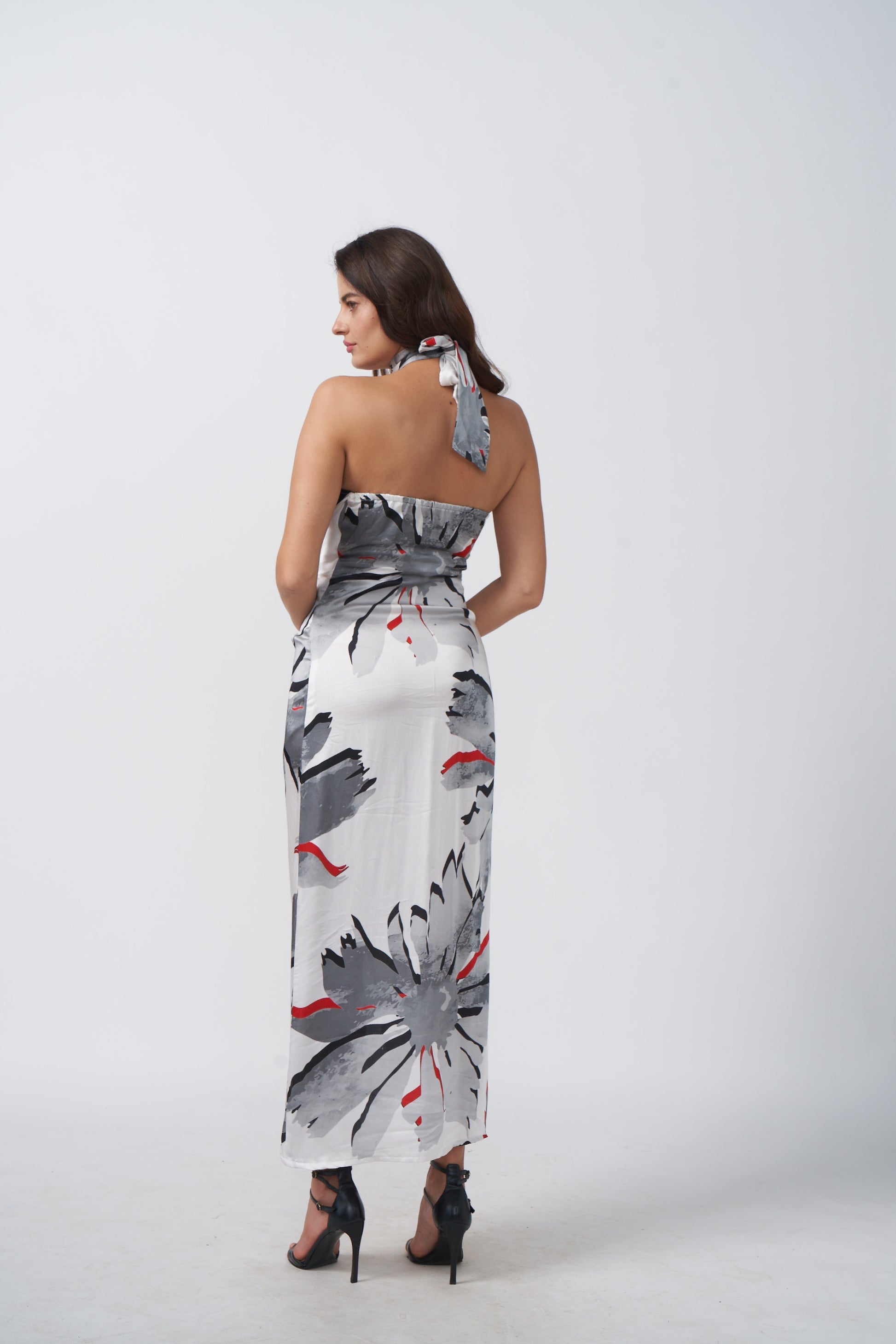 Back view of model wearing satin halter dress with tie-back and wrap silhouette in grey floral print.