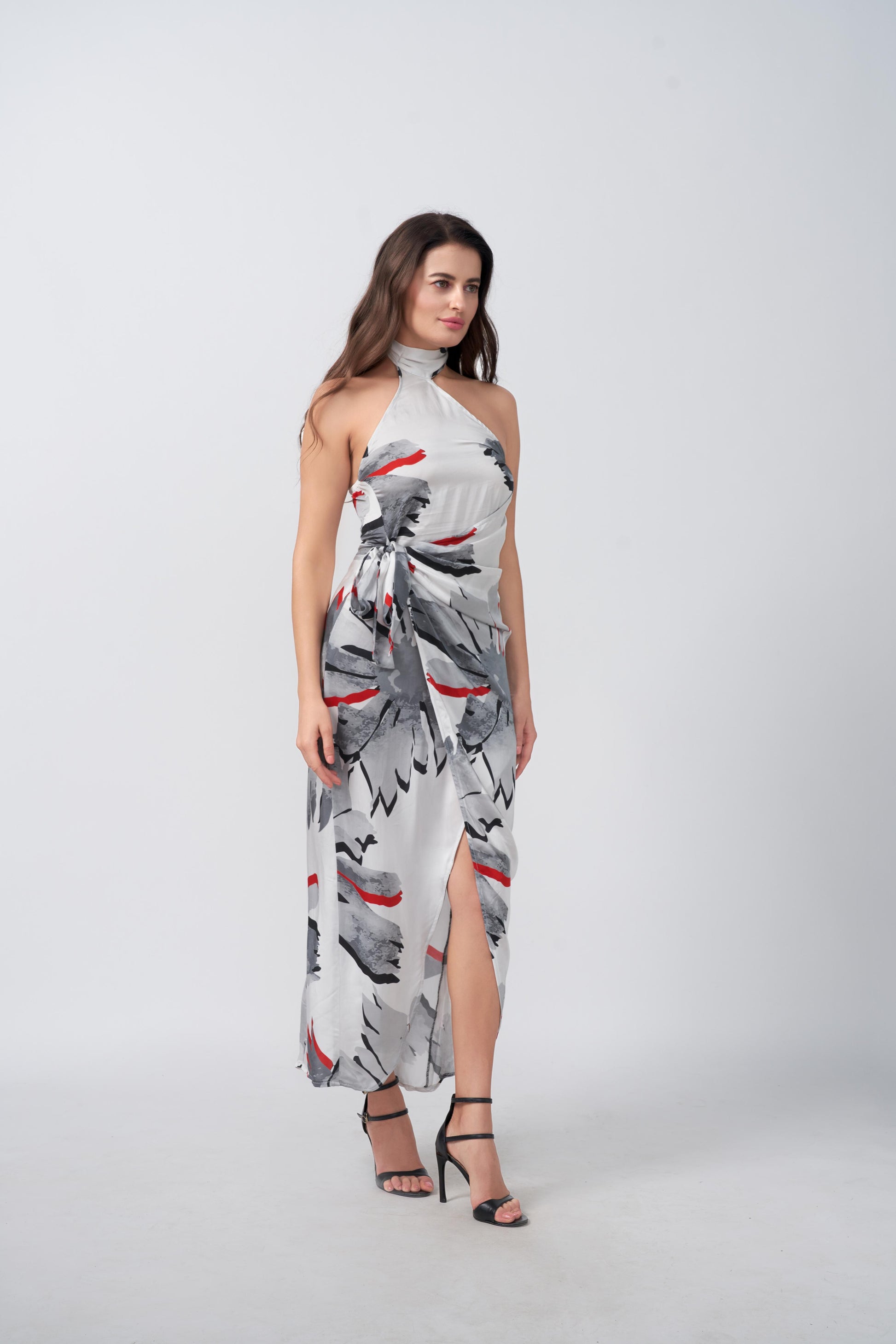  Side view of model walking in satin wrap dress featuring a grey floral print and subtle red accents.