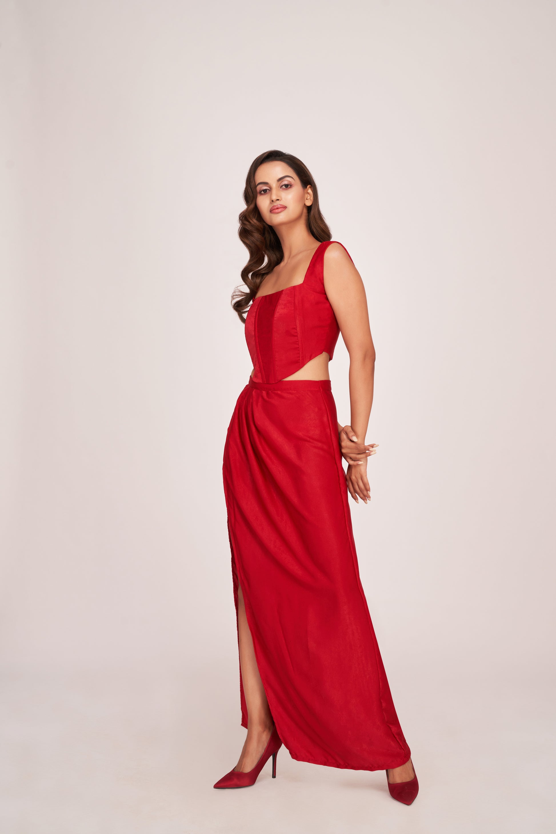 Red co-ord outfit styled with an angled pose, showing the corset top’s snug fit and dramatic skirt slit with U-shaped hem.