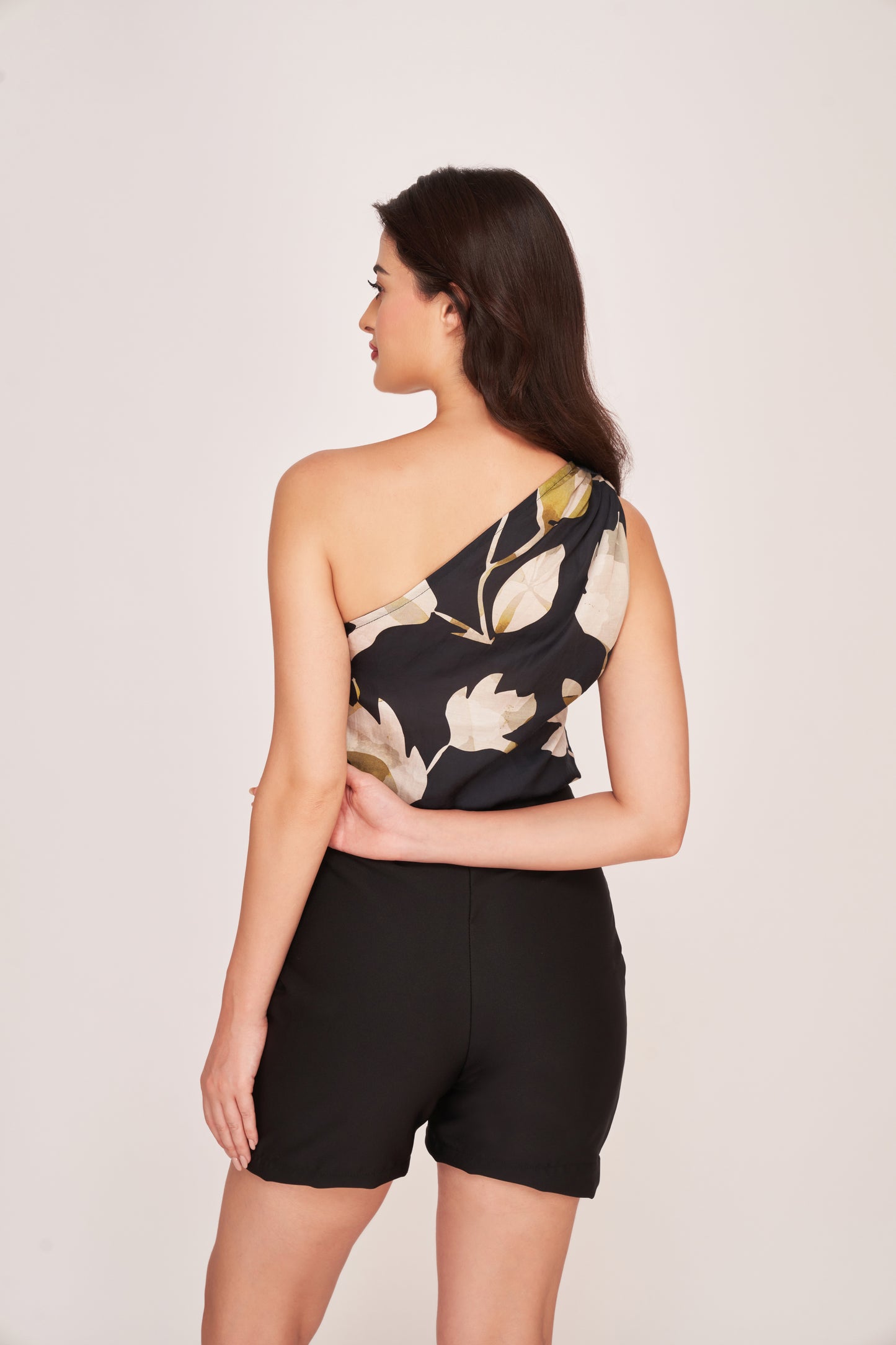 Side profile view of the black floral one-shoulder co-ord set, highlighting the soft drape of the satin fabric and the sculpted silhouette.