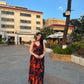 Side view of a woman wearing a red and black floral chiffon dress with spaghetti straps, posing outdoors