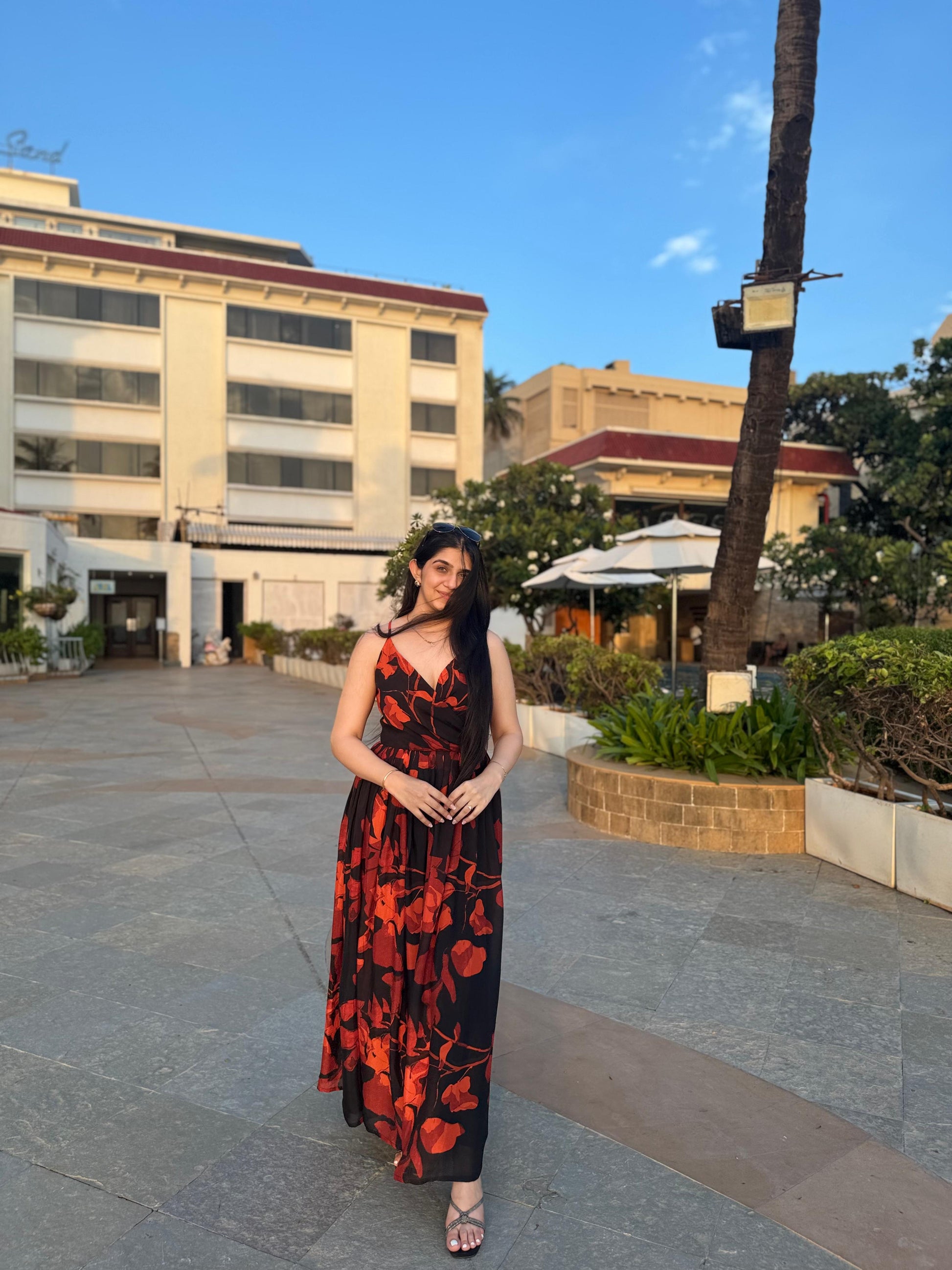 Side view of a woman wearing a red and black floral chiffon dress with spaghetti straps, posing outdoors