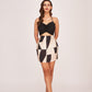 Model facing forward in a black and white abstract silk mini dress with sweetheart ruched neckline, posing with both hands placed behind her back.