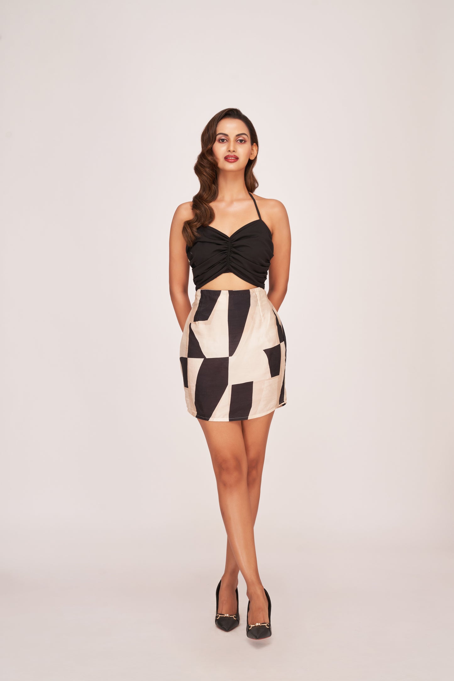 Model facing forward in a black and white abstract silk mini dress with sweetheart ruched neckline, posing with both hands placed behind her back.