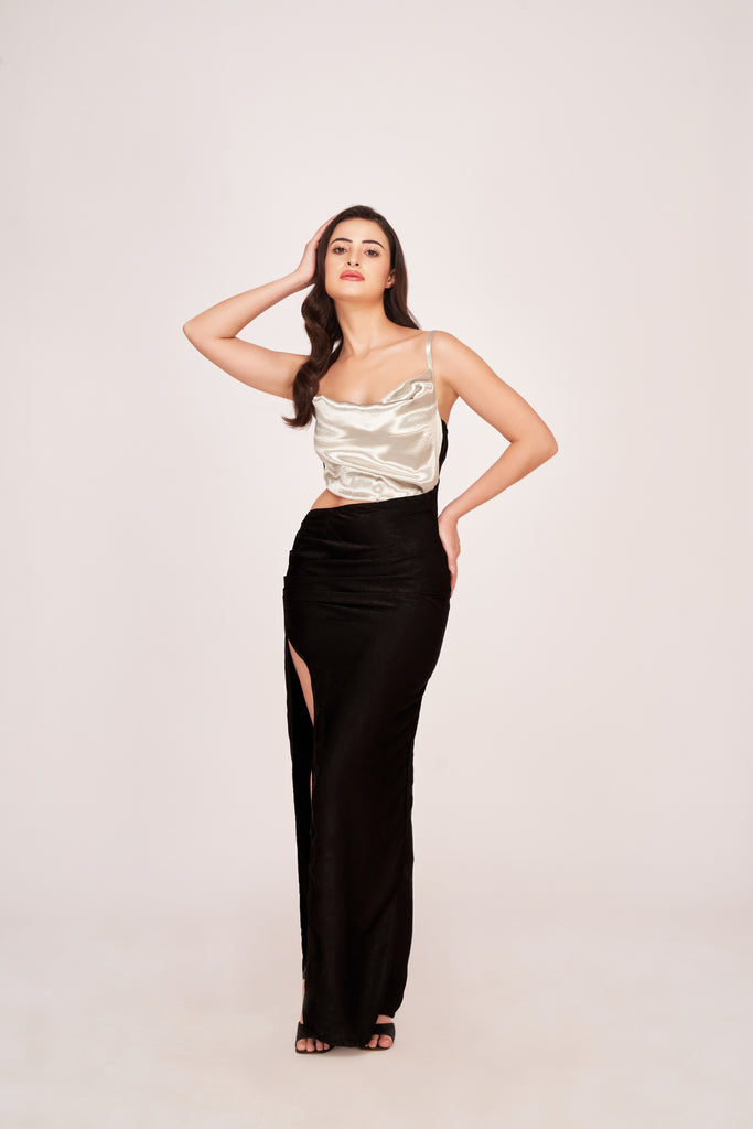 Model in an ankle-length silver and black satin dress with cowl neck and high slit, standing confidently.