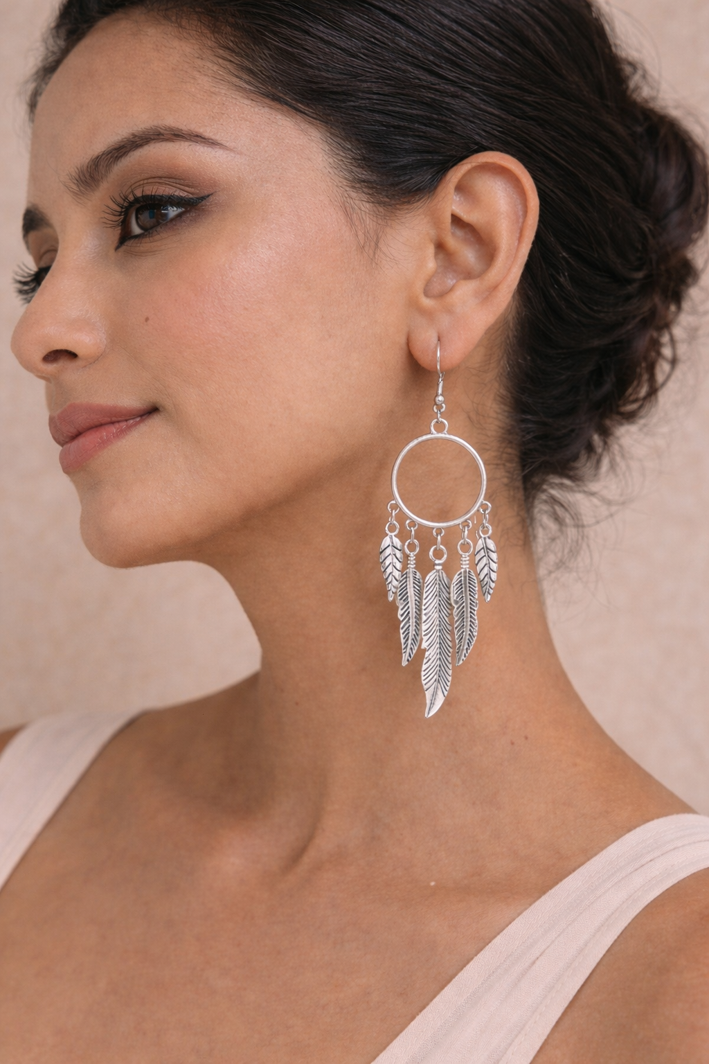 A woman wearing bohemian silver Feather Hoop Drop Earrings featuring a circular hoop with multiple dangling metallic feather charms.