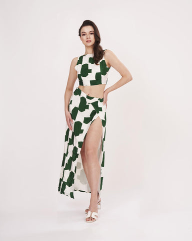 Confident front-facing pose with one hand on waist, emphasizing the round neckline and skirt print of the green co-ord.
