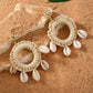 Bohemian imitation gold Shell Ring Drop Earrings featuring dangling white cowrie shells on woven straw hoops, displayed on a natural sand background.