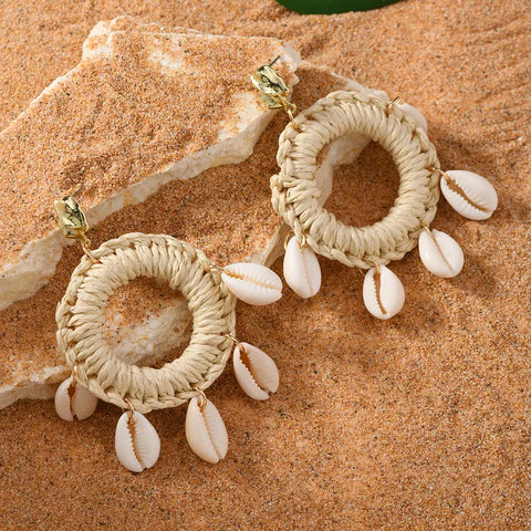 Bohemian imitation gold Shell Ring Drop Earrings featuring dangling white cowrie shells on woven straw hoops, displayed on a natural sand background.