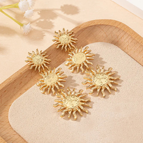 A pair of stunning gold-toned drop earrings featuring a circular sunburst motif with delicate, textured rays extending from the center