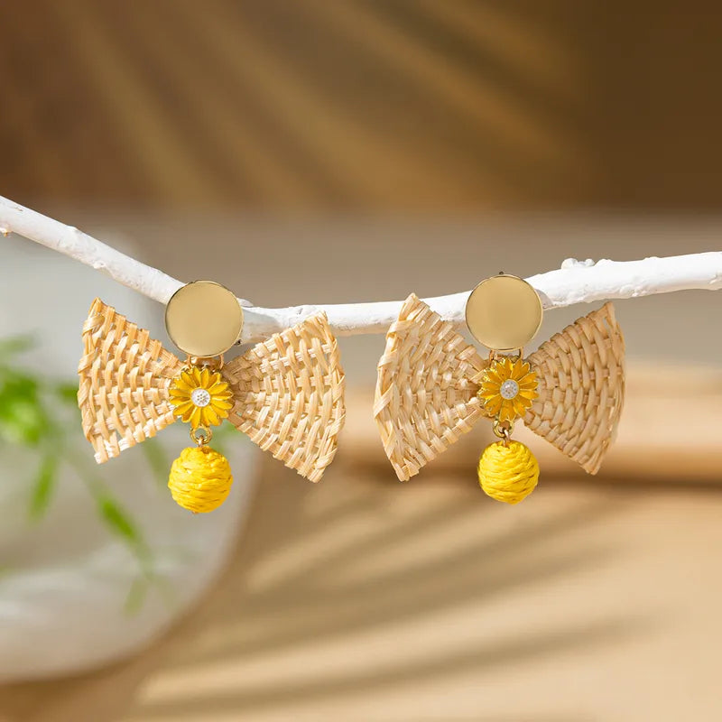 Boho-style woven raffia bow earrings with yellow sunflower details, in the middle. A cheerful accessory ideal for summer vacations or garden parties.