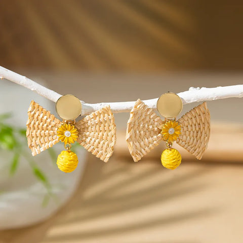 Boho-style woven raffia bow earrings with yellow sunflower details, in the middle. A cheerful accessory ideal for summer vacations or garden parties.