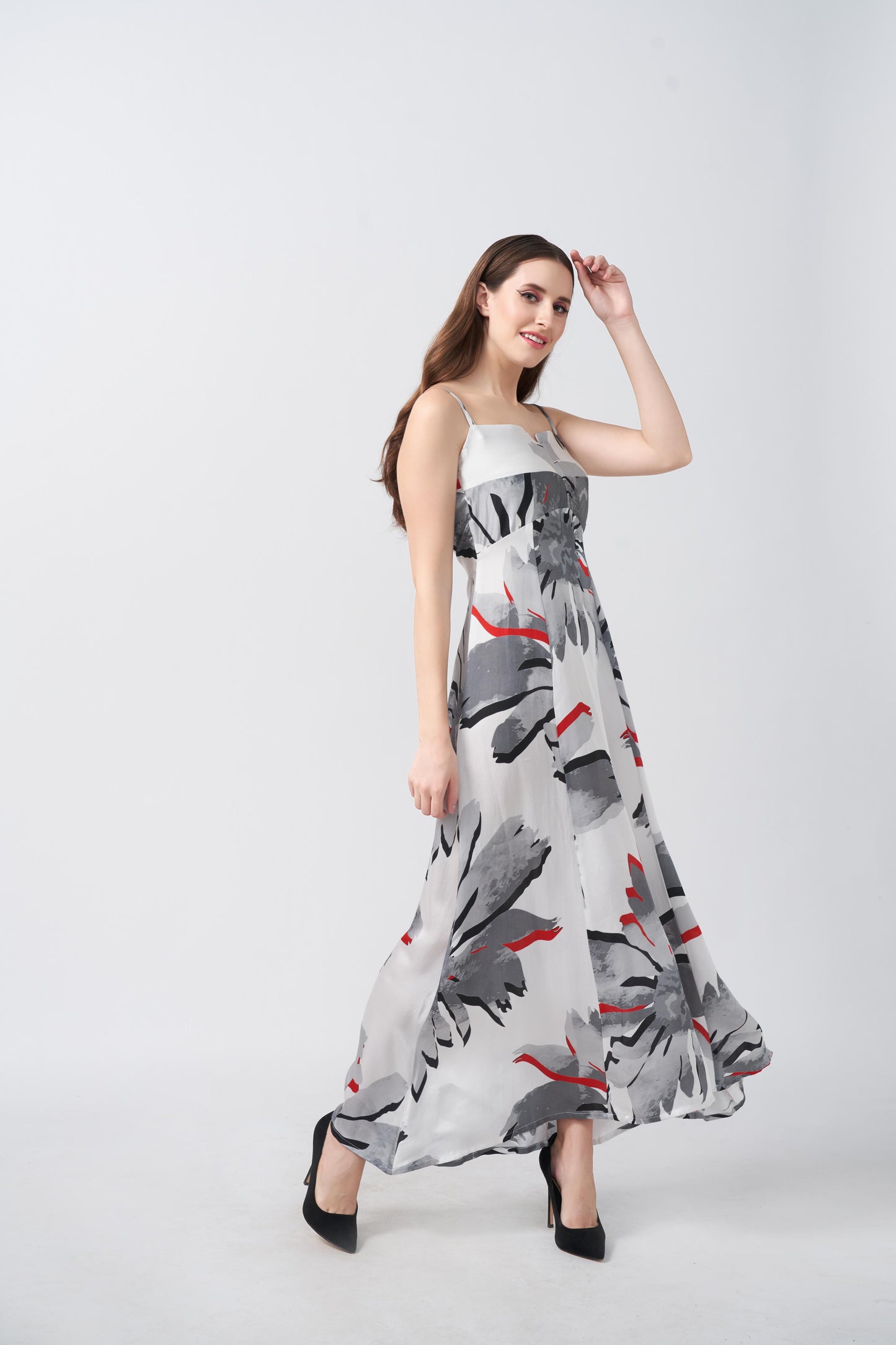 Model twirling in a flowy ankle-length satin dress with square neckline and red-accented floral design.