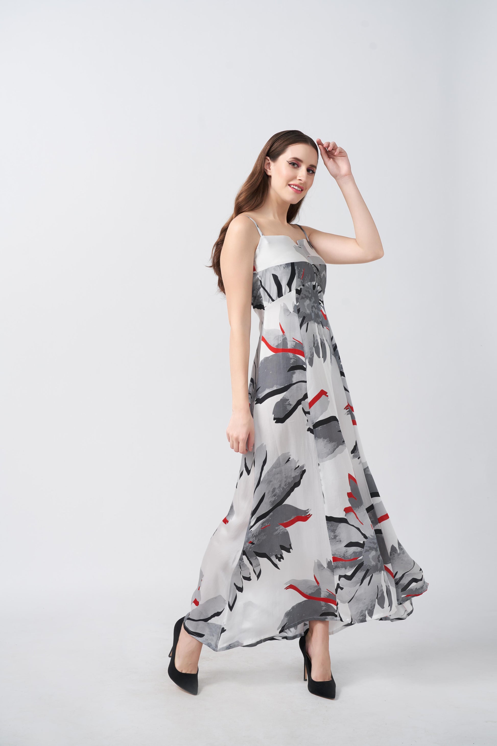 Model twirling in a flowy ankle-length satin dress with square neckline and red-accented floral design.