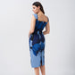Model in motion, turning slightly to showcase the side drape and flattering silhouette of the printed blue midi dress.