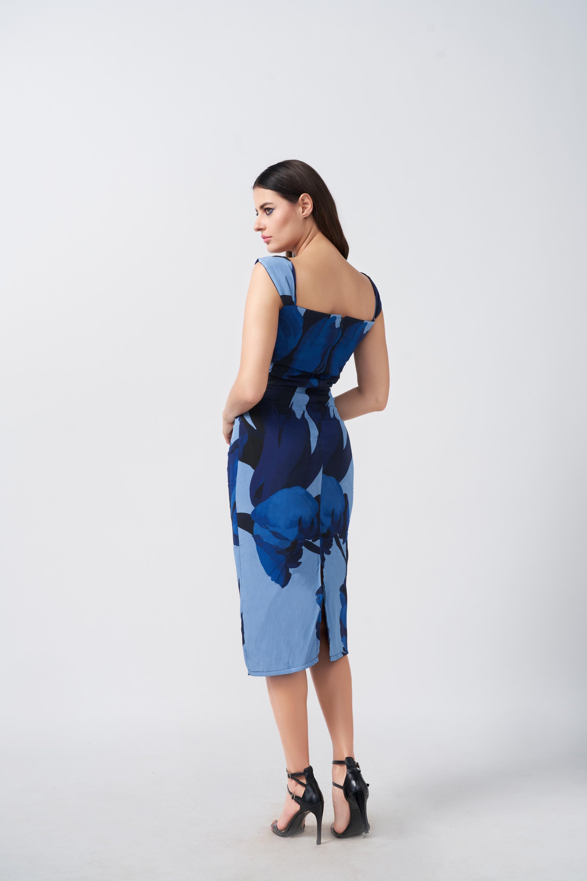 Model in motion, turning slightly to showcase the side drape and flattering silhouette of the printed blue midi dress.