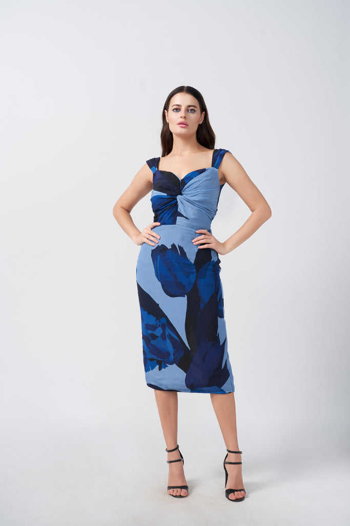 Model posing front-facing in a sleeveless midi dress with twisted neckline and blue floral print, showcasing the flattering fit.