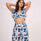Model with both arms raised above her head highlighting the deep V-neckline and fitted waist of the printed crop top.