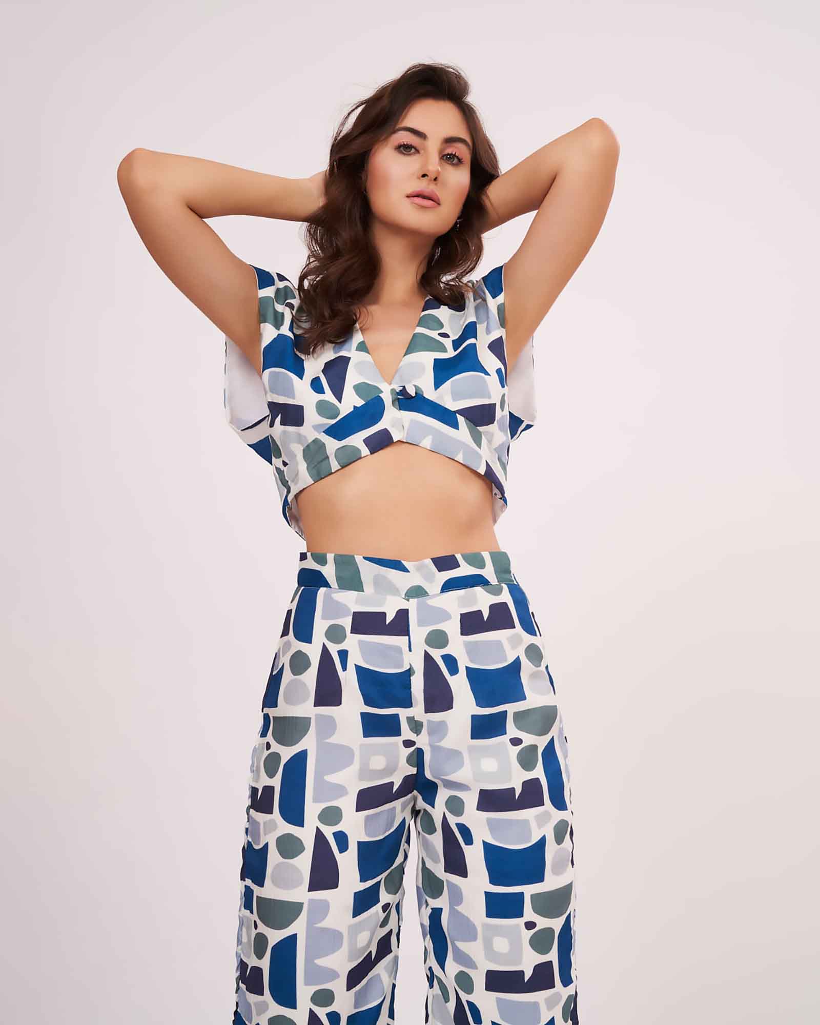 Model with both arms raised above her head highlighting the deep V-neckline and fitted waist of the printed crop top.
