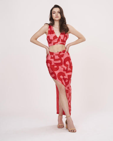 Hands-on-waist pose highlighting the deep V-neck and slit placement on the red printed skirt set.