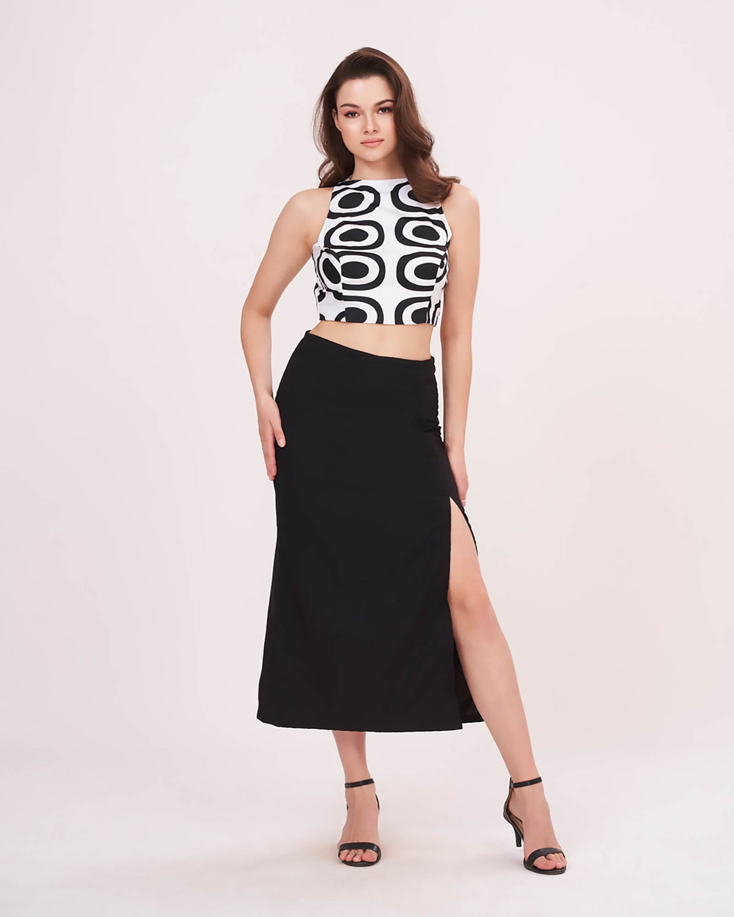 Model in a confident front-facing pose wearing the abstract printed white top and black thigh-high slit skirt.