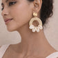 A woman wearing large bohemian Shell Ring Drop Earrings featuring white cowrie shells attached to a woven straw hoop with a gold-tone stud.