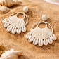 A pair of stunning statement earrings featuring a natural cowrie shell stud and a large, circular drop woven from white raffia.