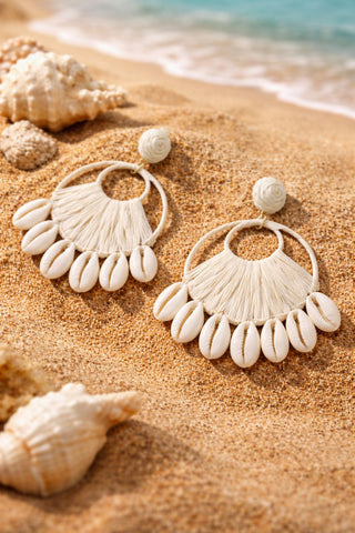 A pair of stunning statement earrings featuring a natural cowrie shell stud and a large, circular drop woven from white raffia.