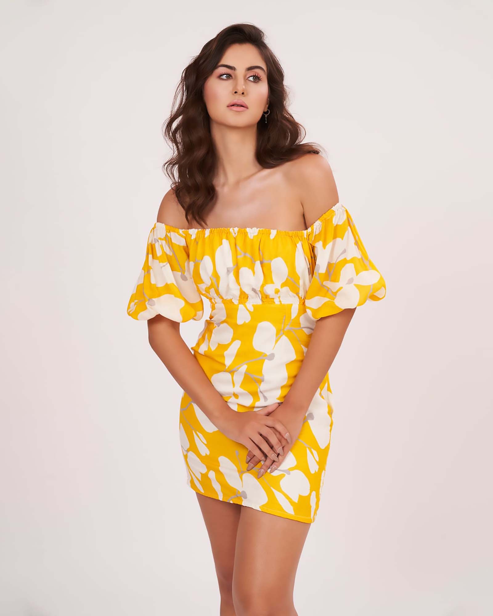 Close-up of model in yellow floral off-shoulder mini dress with puff sleeves, hands held gracefully in front.
