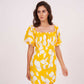 Walking pose of model in yellow printed dress, showcasing movement and flared silhouette with puffed sleeves.