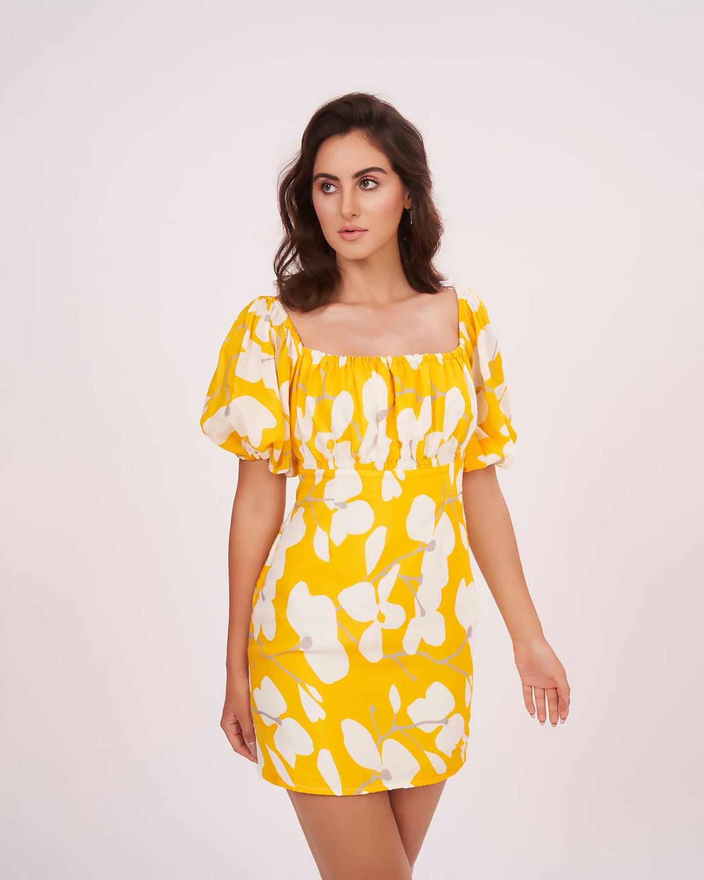 Walking pose of model in yellow printed dress, showcasing movement and flared silhouette with puffed sleeves.