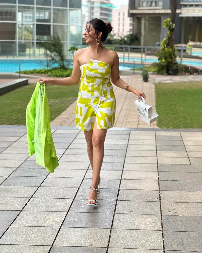 Model walking by the poolside in a vibrant yellow printed tube dress, styled with a shrug and heels.