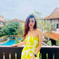 Model in the outdoors in the yellow printed dress, emphasizing the strapless neckline and vacation-ready feel.