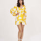 Front-facing view of model in yellow abstract print satin wrap dress with balloon sleeves.