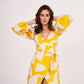 Model with arms on her head in yellow satin wrap dress, highlighting sleeve volume and flow.