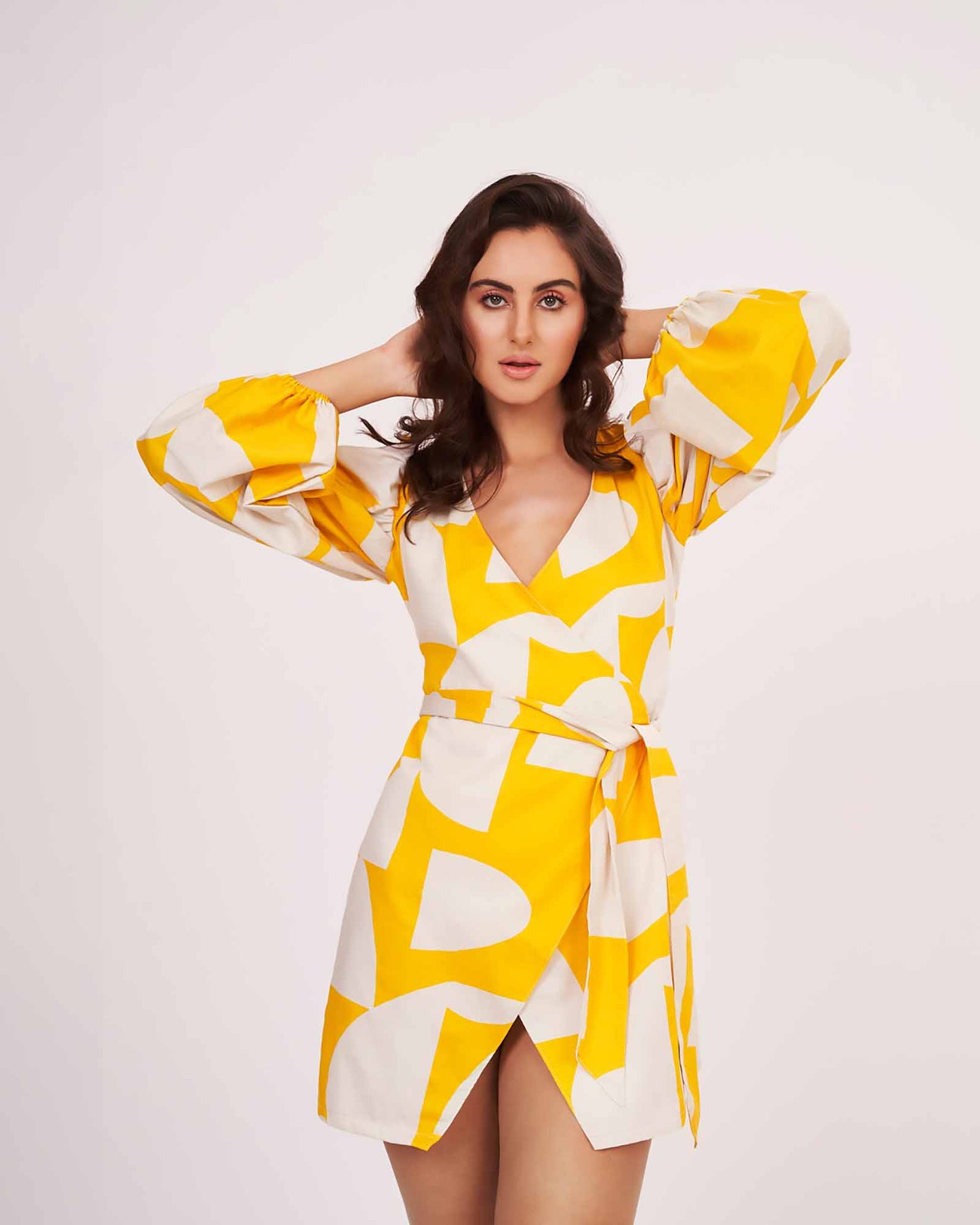 Model with arms on her head in yellow satin wrap dress, highlighting sleeve volume and flow.