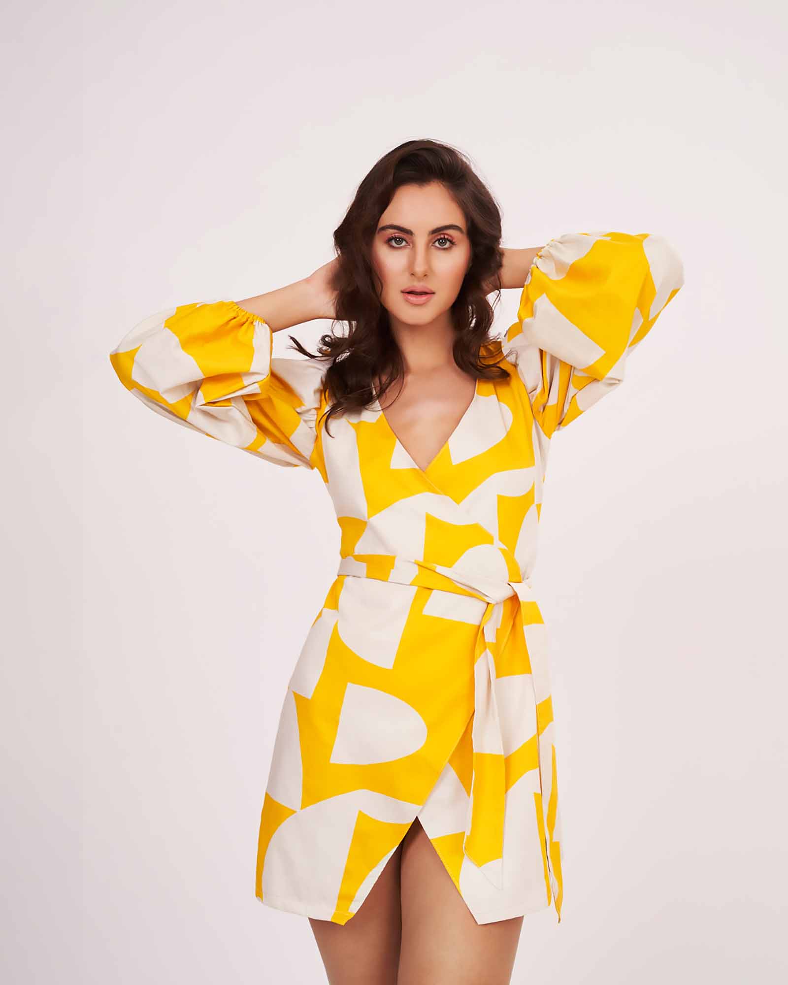 Model with arms on her head in yellow satin wrap dress, highlighting sleeve volume and flow.